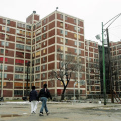 A mid-rise public housing building with people walking in the foreground